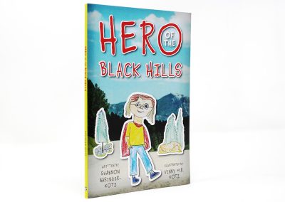 Hero of the Black Hills book photo, showing illustrated sticker cutouts of a boy and some trees on top of a photo of the black hills