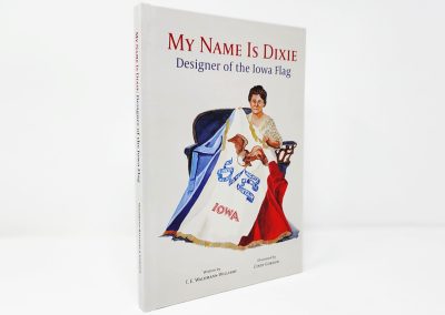 My Name Is Dixie book photo, showing a white cover with the title in red and blue at the top and an illustration of Dixie holding the Iowa flag at the bottom