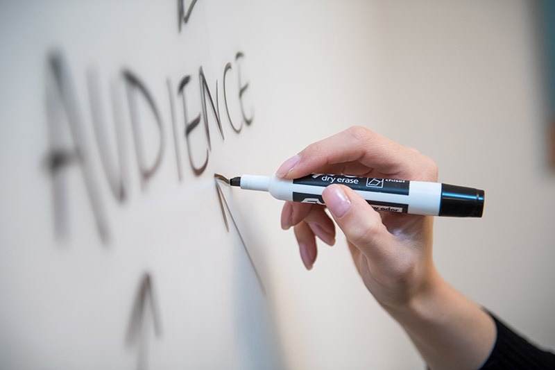 Hand writing the word "Audience" on a whiteboard