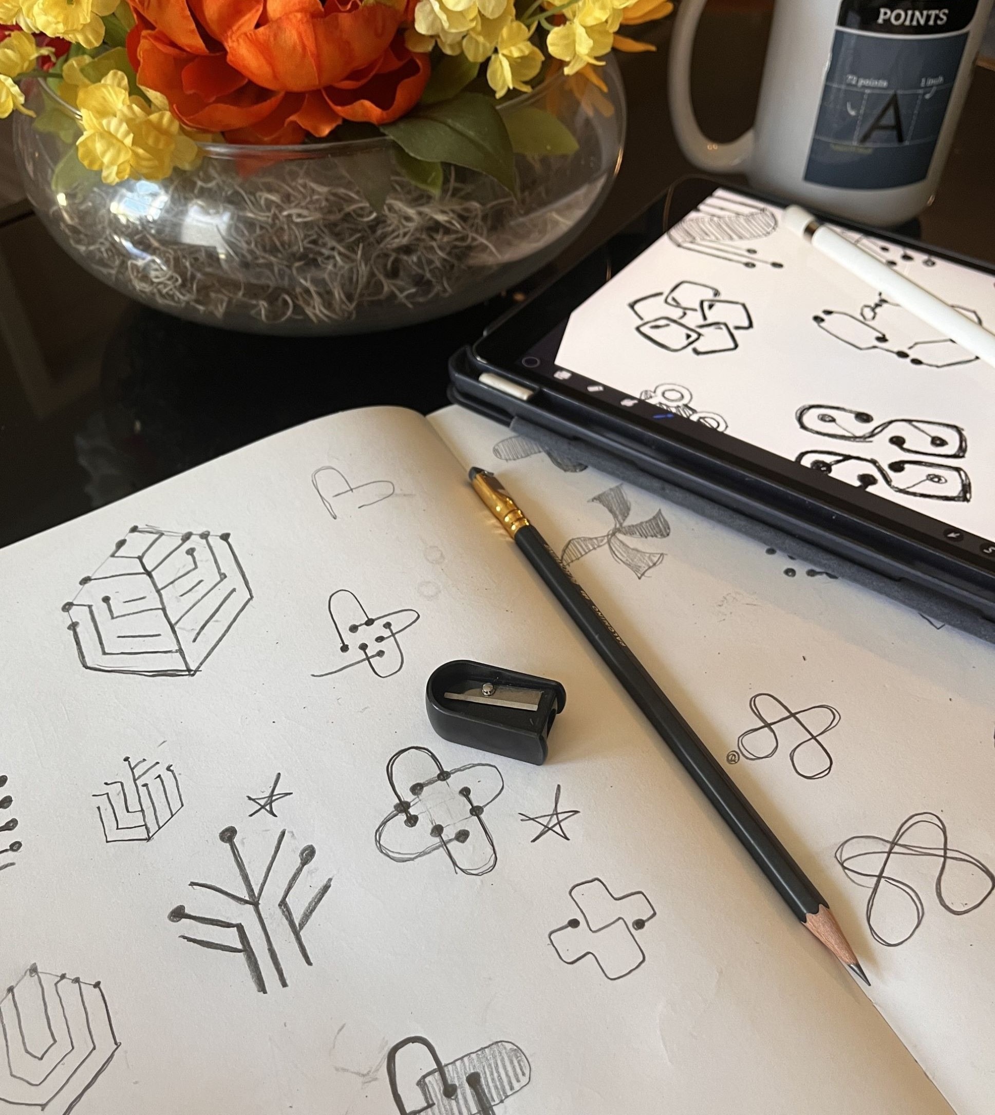 Sketchbook with NCPDP Foundation logo sketches on table with pencil, mug, and flowers